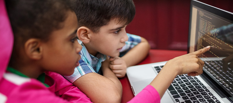 An image of a girl and boy pointing to the screen of an open laptop